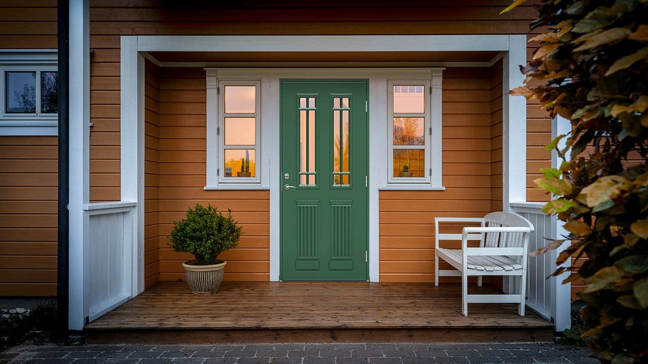 Gult hus med hvite detaljer og grønn ytterdør med glassfelt med overbygg.
