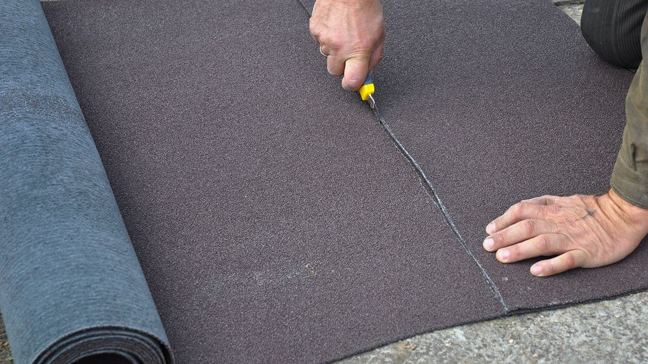 Håndverker som kutter en rull med takpapp.