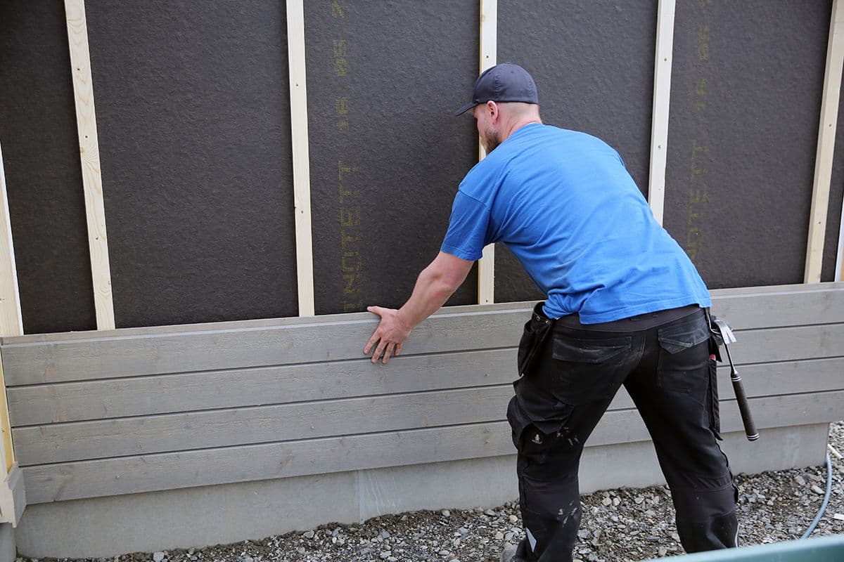 mann fester ny kledning på en yttervegg