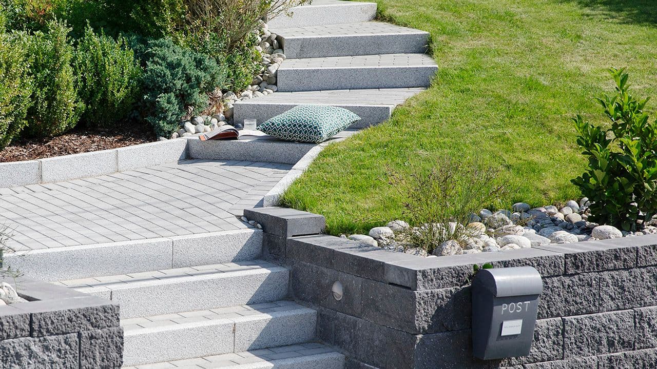 Hage med steinbed inspirasjon. Et steinbed med elvestein og et blomsterbed kantstein i hage med trapp..