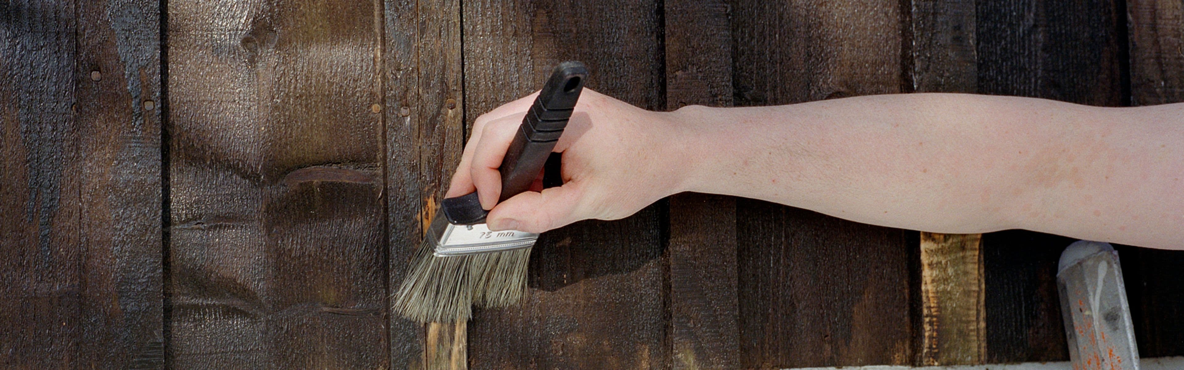 Nærbilde av hånd med pensel som skal male hus utvendig.