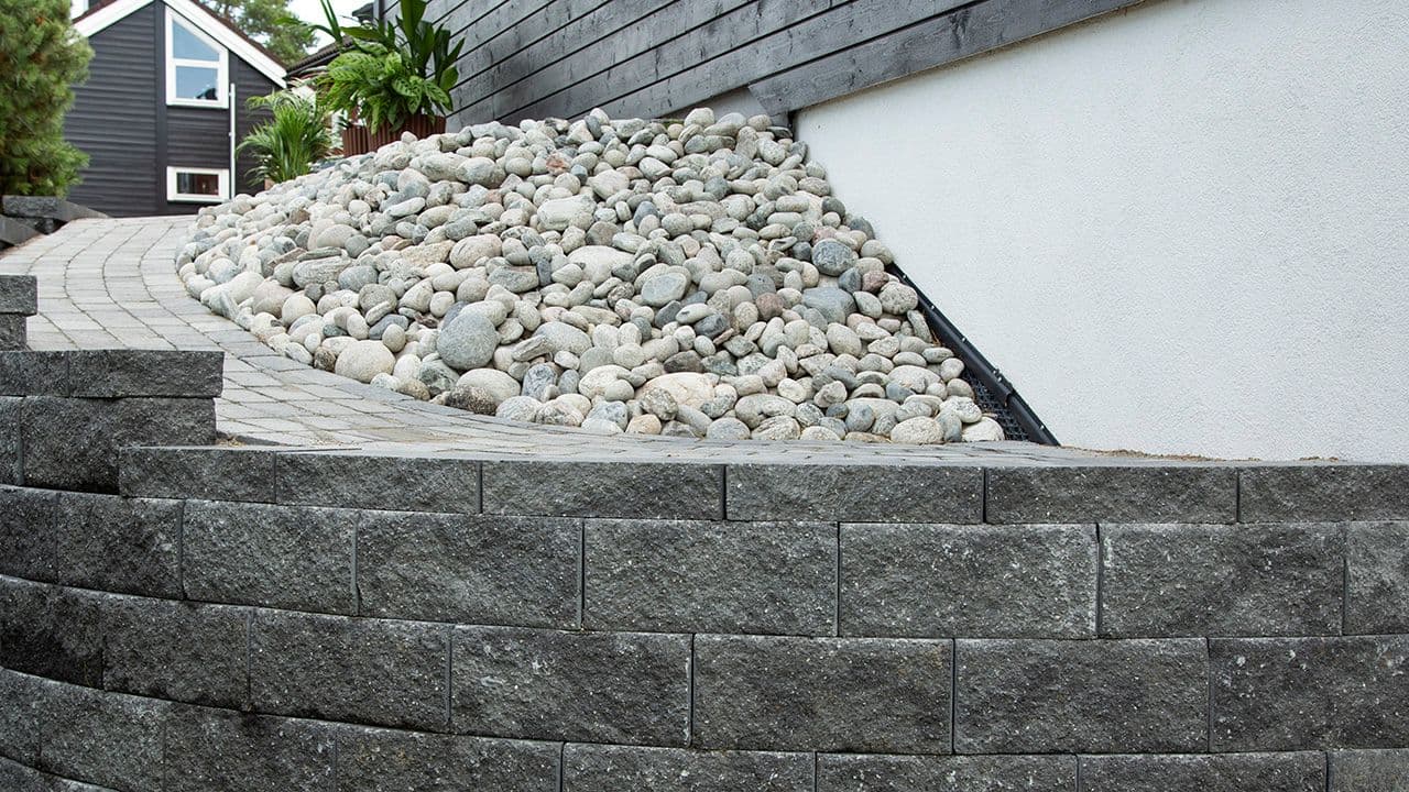 Elevstein i skråning med gangsti ved husvegg.