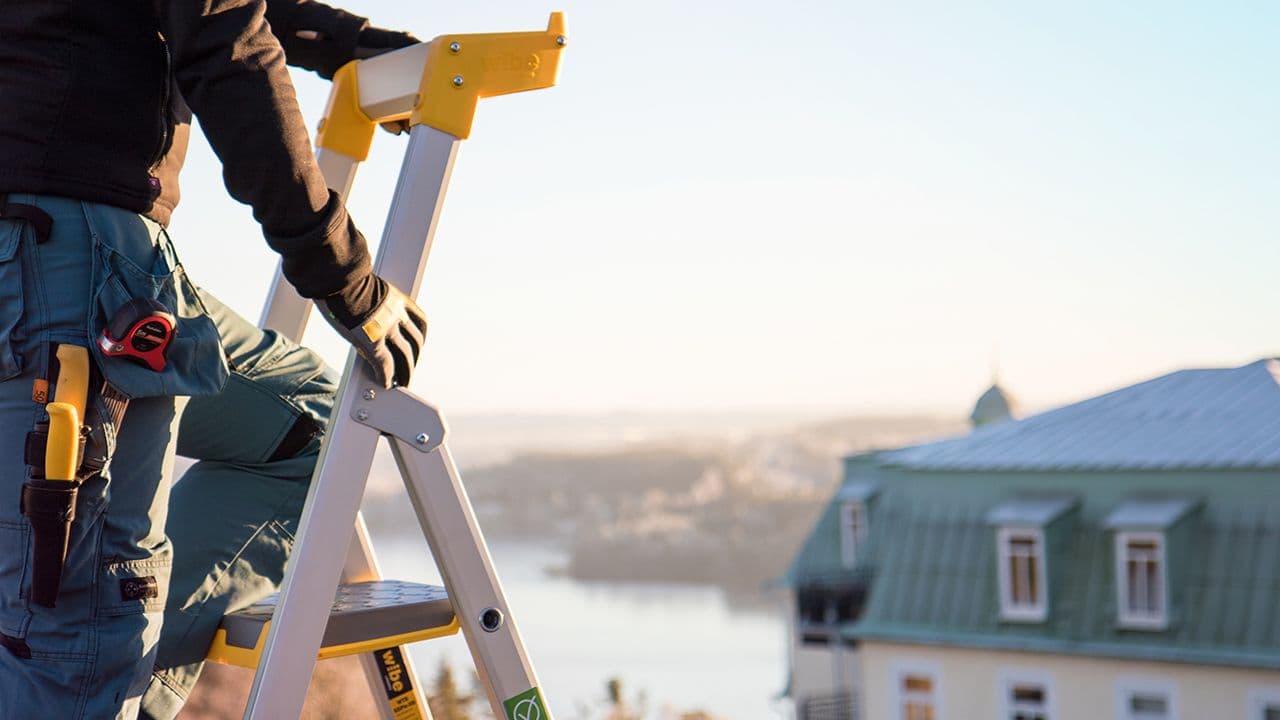 Håndverker som holder seg fast i stige når han arbeider i høyden.