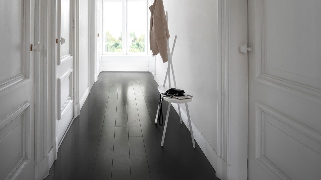 Smal gang med hvite vegger og svart parkettgulv.