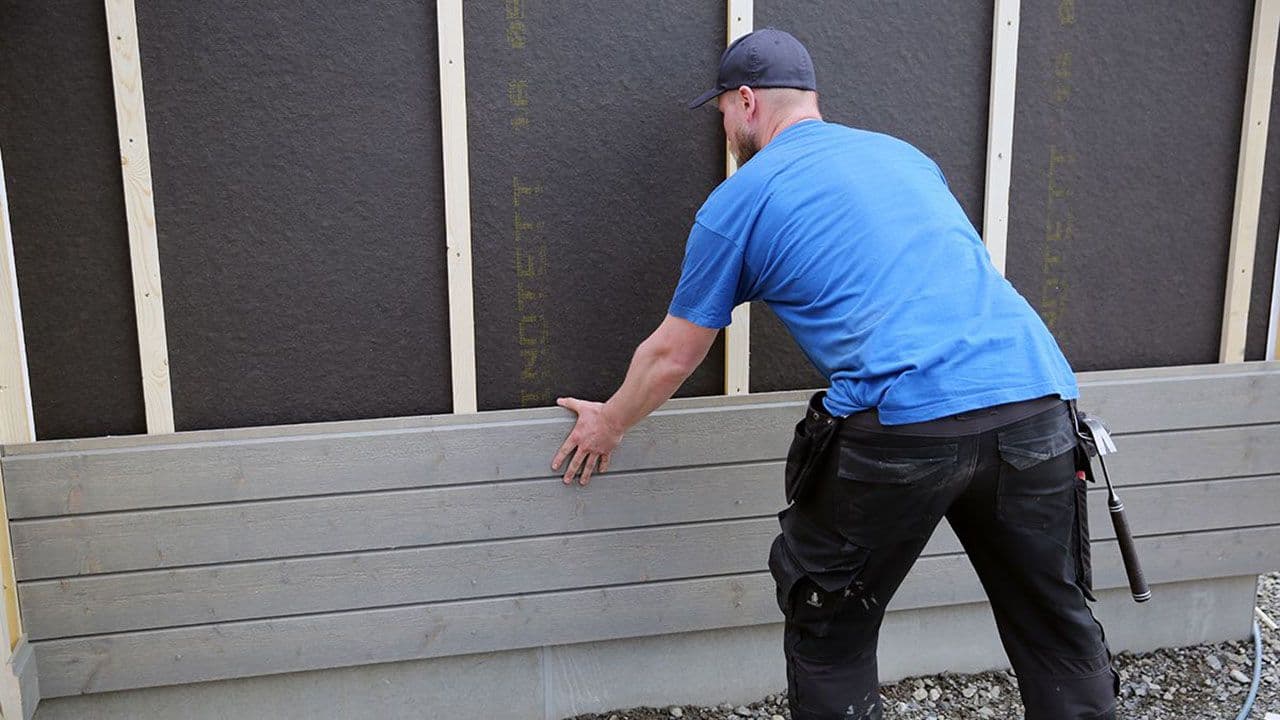 Mann som etterisolerer yttervegg ogmonterer ny kledning på en yttervegg.