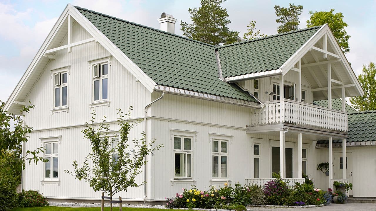 Moderne kledning på hus i hvitt med grønn takstein.