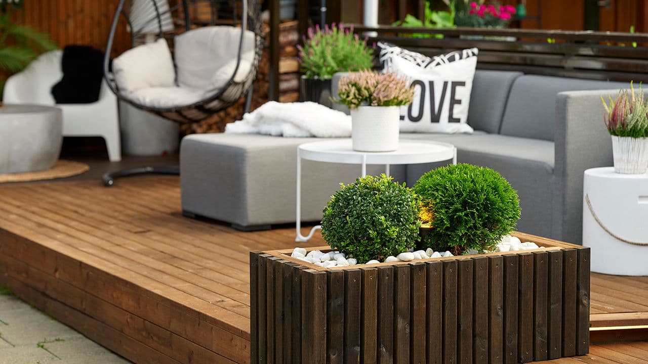 Brun terrasse med hagemøbler og grønne planter.