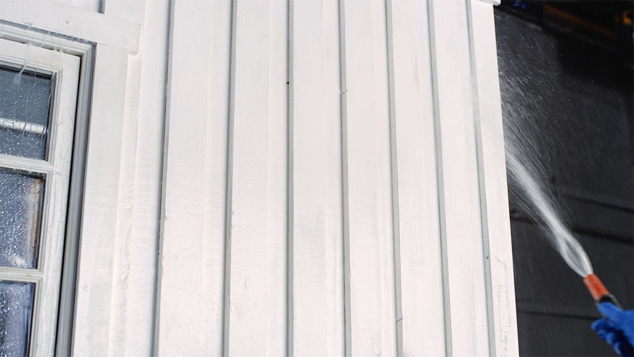 Husvegg som blir spylt med hageslange for å vaske huset før maling.