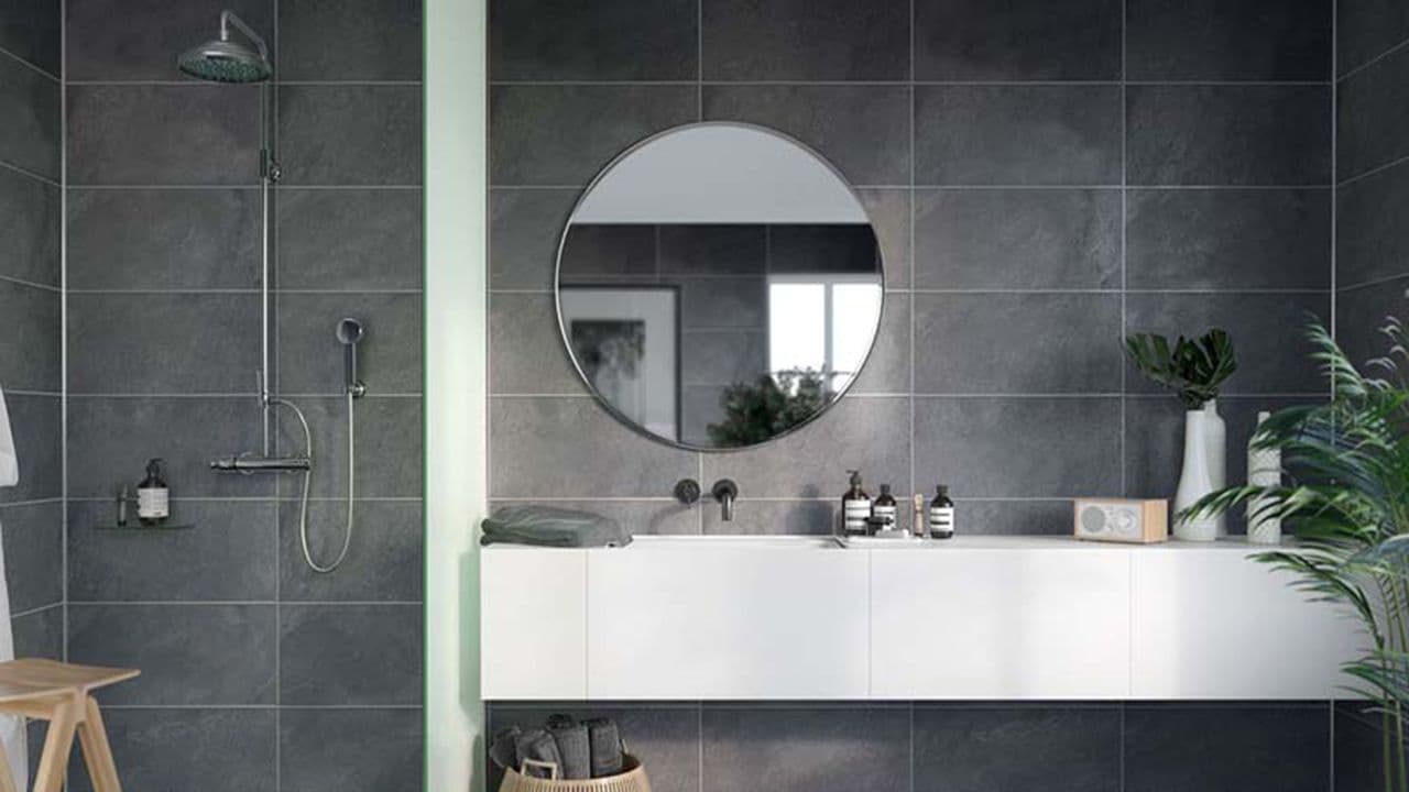 Grå baderomsplater på bad med dusj og hvite baderomsmøbler.