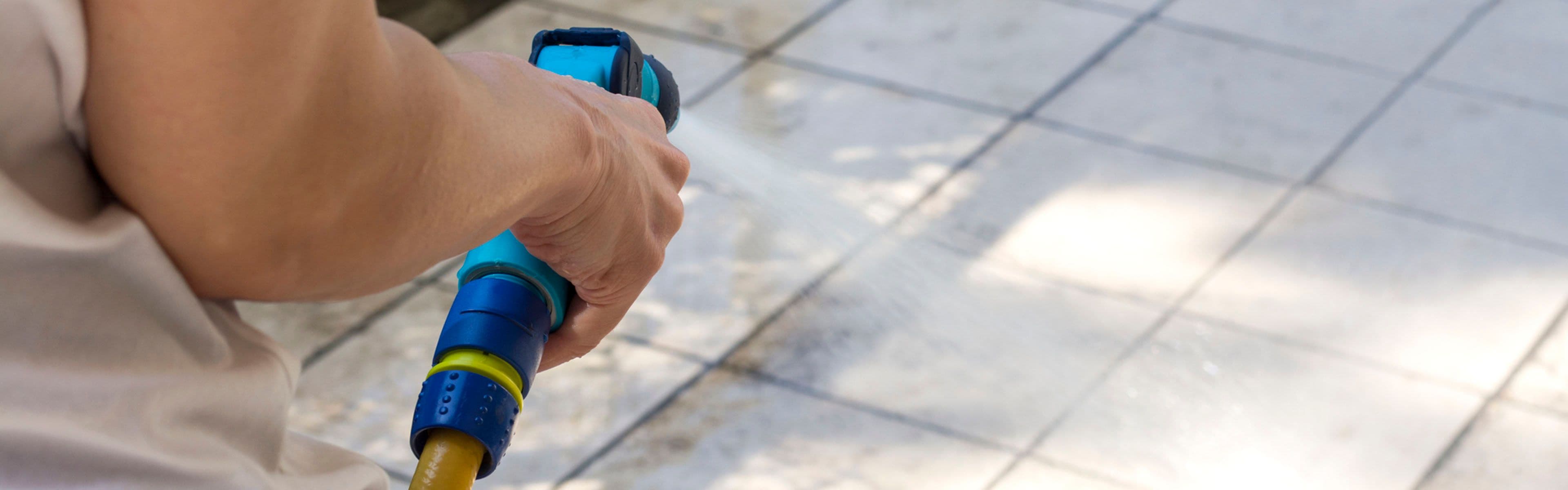 Person som vasker steinfliser med hageslange.