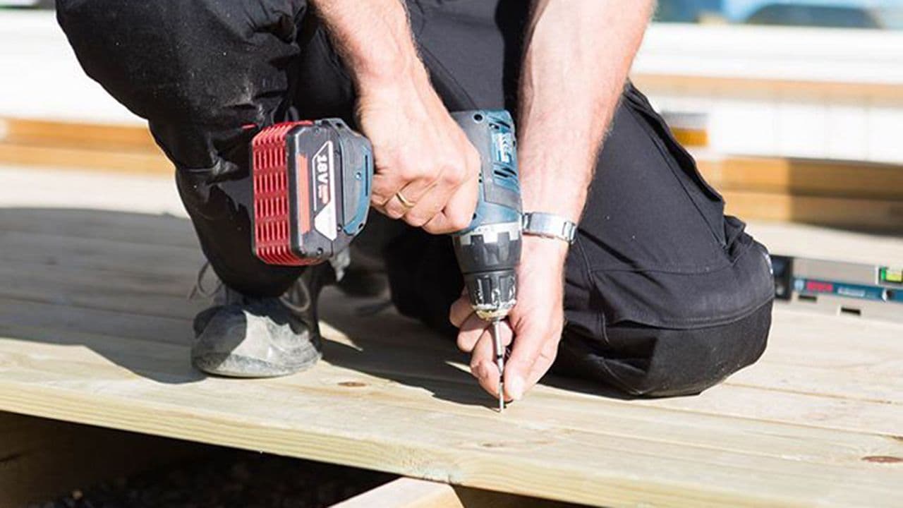 Håndverker som holder på å bygge platting med drill som verktøy.