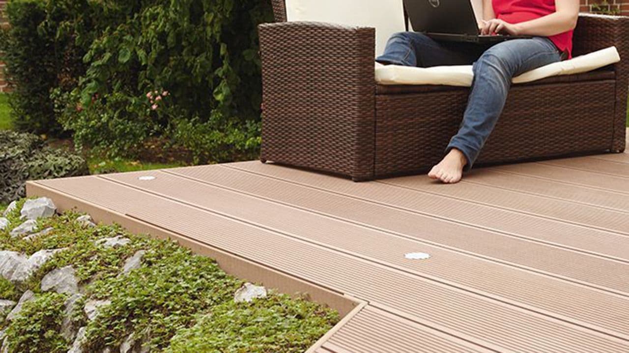 Kvinne som sitter på PC i hagesofa på terrasse av kompositt terrassebord.