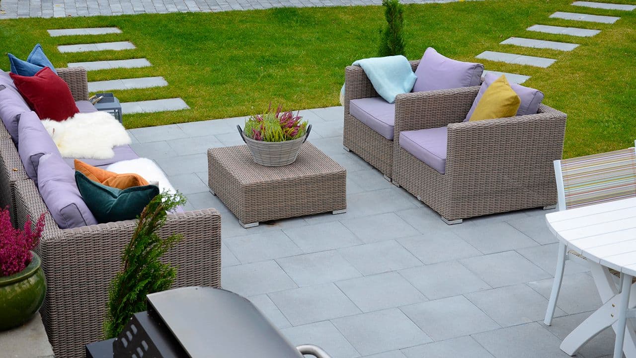 Hage med steinheller på plen og rottingmøbler på stenlagt uteplass.